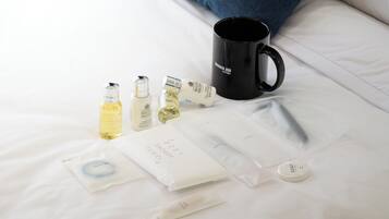 Toiletries on a bed, including a black mug, bottles of lotion, and a vanity kit.