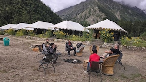 Un groupe de personnes assises sur des chaises à l’extérieur, avec des tentes en arrière-plan.