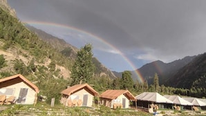 Une rangée de cabanes avec une chaîne de montagnes en arrière-plan et un arc-en-ciel.
