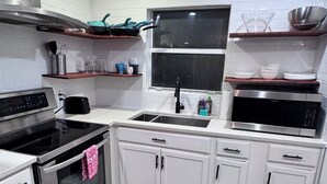 A modern kitchen with white cabinets, a stainless steel oven, a microwave, and a window above the sink. - Compact 3 bed/1bath house 4 miles away from Downtown (Dallas)