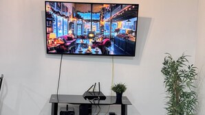 A modern living room with a flat-screen TV mounted on the wall, a black entertainment unit with electronic devices, a marble coffee table, and a potted plant. - Compact 3 bed/1bath house 4 miles away from Downtown (Dallas)