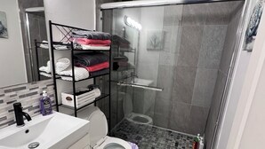 A modern bathroom with a glass-enclosed shower, a white toilet, and a vanity with a sink and soap dispenser. - Compact 3 bed/1bath house 4 miles away from Downtown (Dallas)