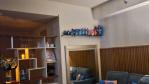 Ein Wohnzimmer mit grauem Sofa, einem flauschigen blauen Teppich und einem Regal mit Plüschtieren.