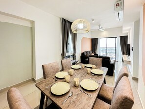 Uma área de refeições moderna com uma mesa posta para seis pessoas, um sofá e uma grande janela com cortinas.