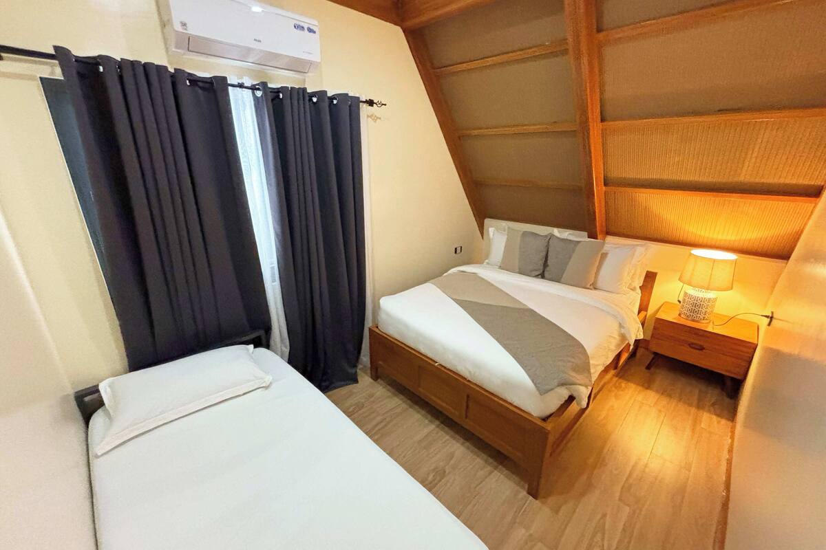 Ein Schlafzimmer mit einem Bett, einem Nachttisch mit Lampe und einem Fenster mit Vorhängen.