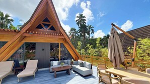Un espace extérieur moderne, aménagé avec une terrasse en bois, une structure triangulaire en bois et offrant une vue sur la végétation environnante.
