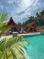 Un resort con piscina, cabañas de madera y vegetación tropical.