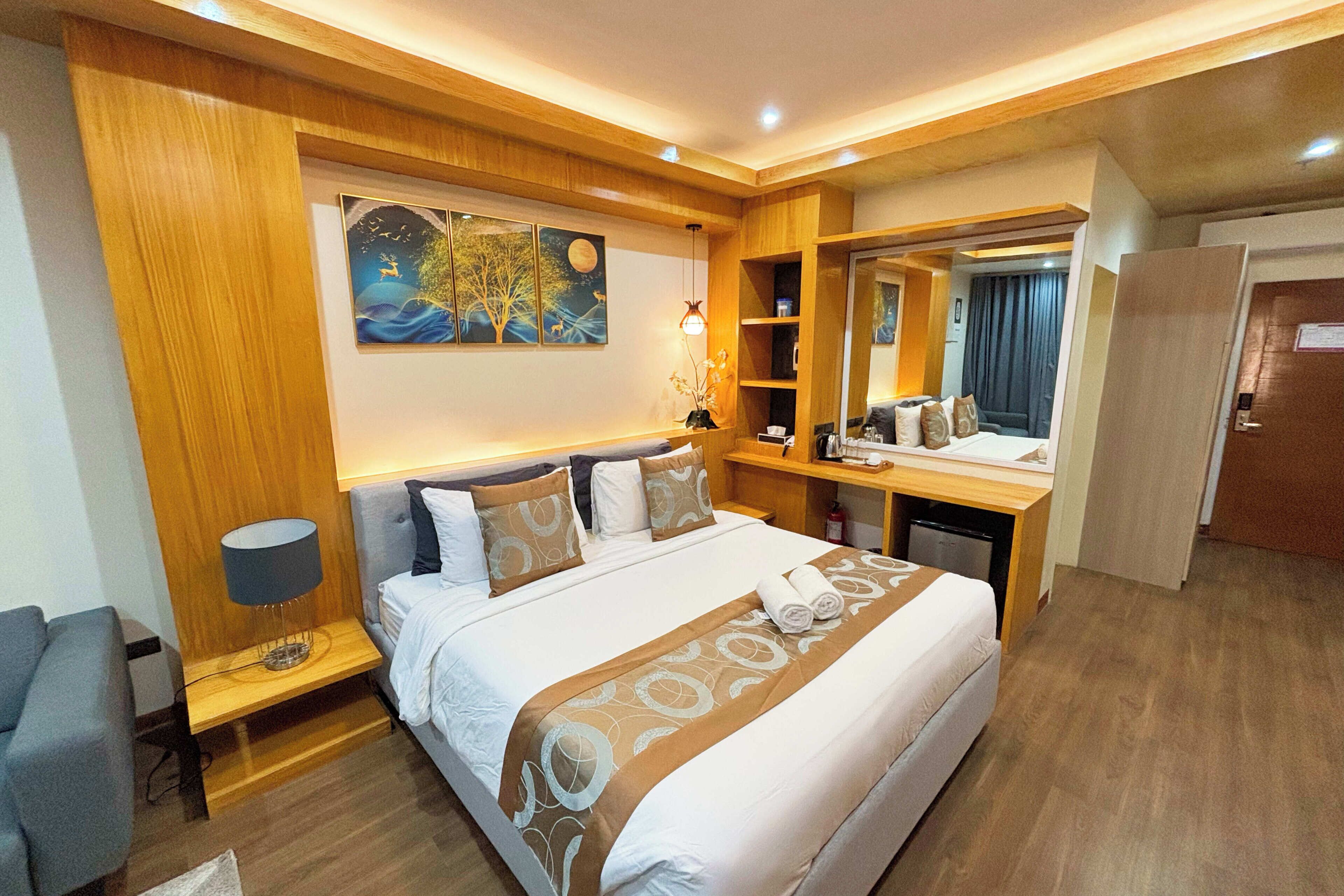 Een hotelkamer met een groot bed, nachtkastjes, een bureau, een stoel, een spiegel en een schilderij aan de muur.