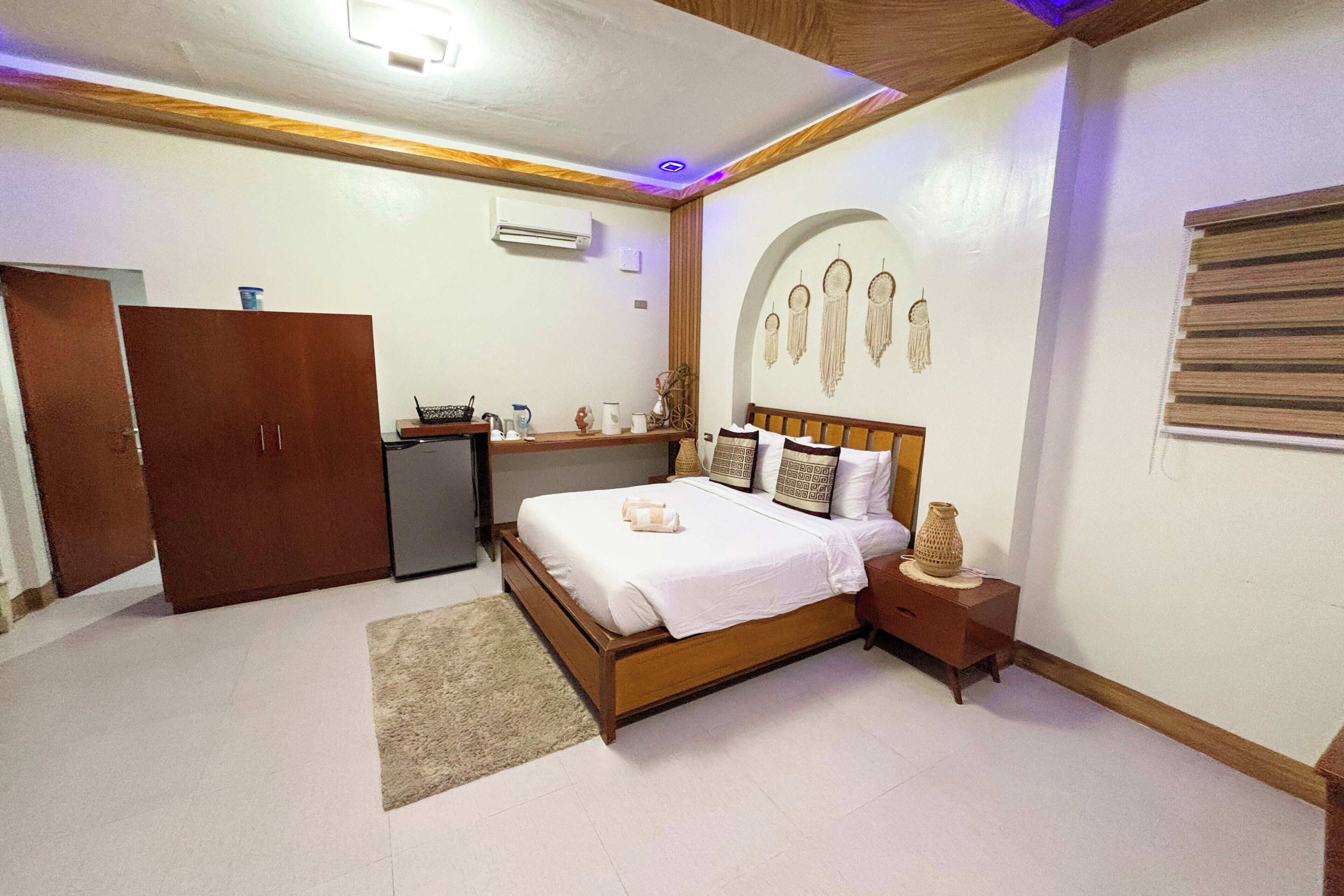 A bedroom with a wooden bed, a nightstand, a dresser, a desk, and a wall with decorative elements.