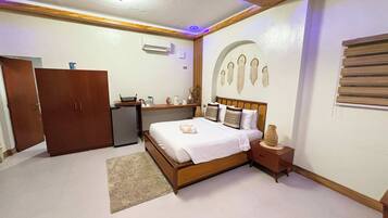 A bedroom with a wooden bed, a nightstand, a dresser, a desk, and a wall with decorative elements.