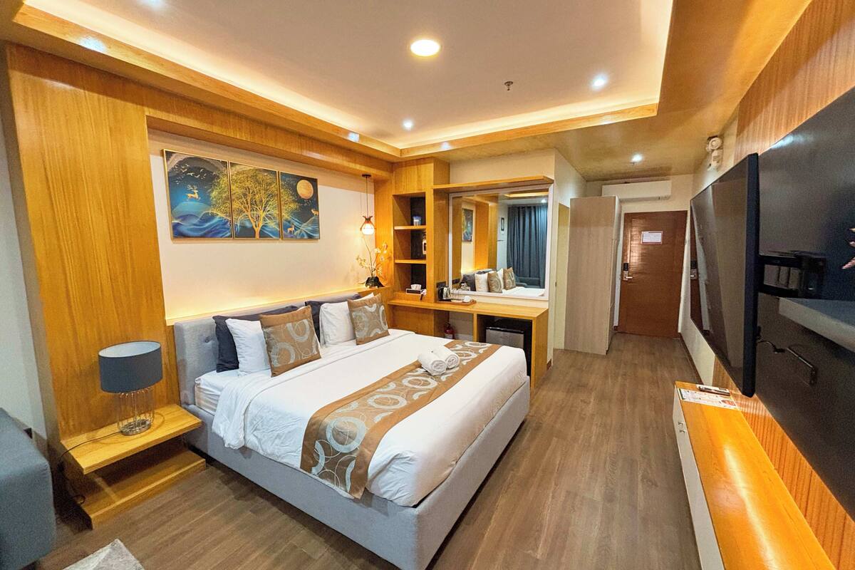 Ein Hotelzimmer mit Bett, Nachttisch, Lampe, Schreibtisch, Spiegel und Fernseher.
