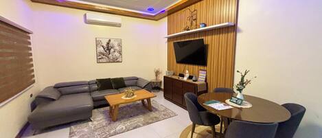 A living room with a sofa, coffee table, TV, and dining area with chairs.