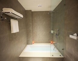 Un baño moderno con ducha de mampara de vidrio, bañera blanca y toallero.
