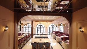 Un'ampia sala da pranzo con soffitti alti, finestre ad arco e diversi tipi di posti a sedere, tra cui tavoli e banconi.