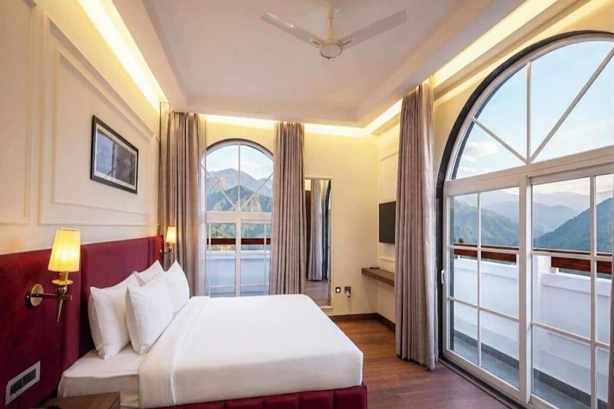 Una habitación de hotel con cama, televisión, ventana con vistas a montañas y ventilador de techo.