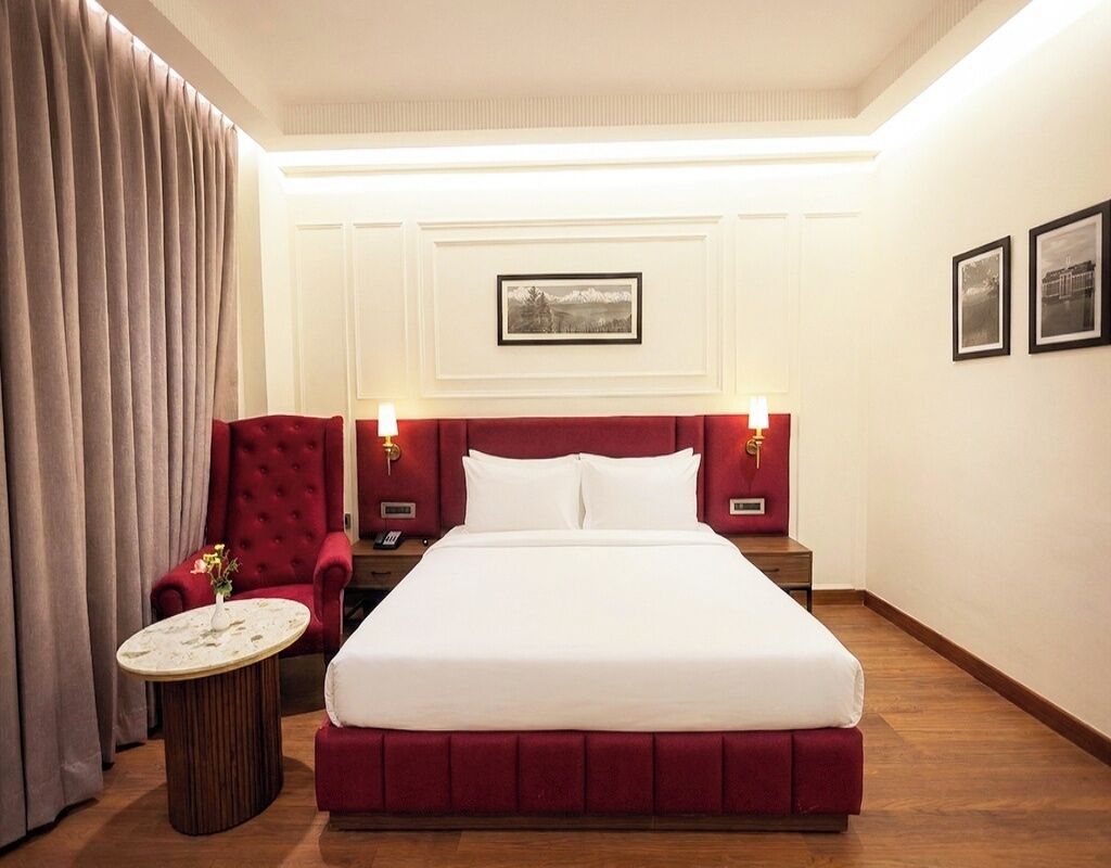 Una habitación de hotel con una cama grande, un sillón rojo, una mesa redonda y dos lámparas de noche.