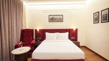 Una habitación de hotel con una cama grande, un sillón rojo, una mesa redonda y dos lámparas de noche.
