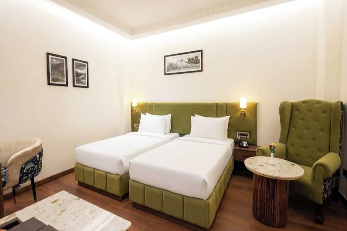 Habitación de hotel con dos camas, un sillón verde, una mesa redonda y cuadros en la pared.