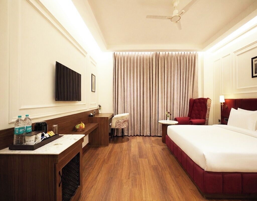 A hotel room with a bed, a desk, a chair, a small table, a TV, and a ceiling fan.