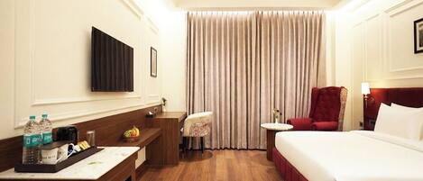 A hotel room with a bed, a desk, a chair, a small table, a TV, and a ceiling fan.