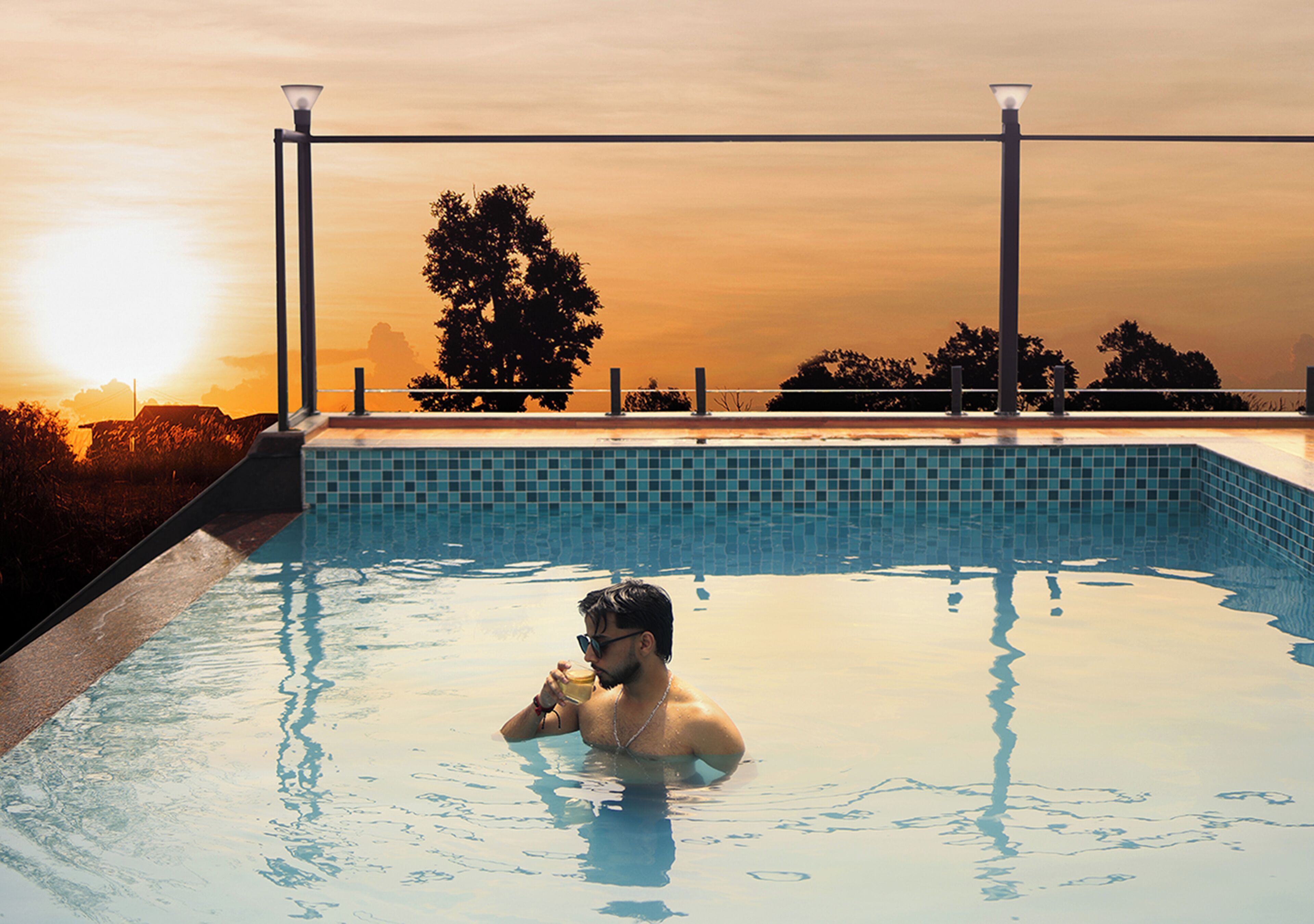 A man in a swimming pool with a sunset in the background.