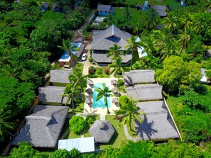 A resort with thatched-roof bungalows, a central swimming pool, and lush tropical vegetation.