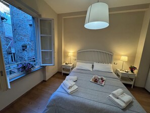 A bedroom with a large bed, two bedside tables with lamps, a window with a view of a building, and a hanging light fixture. - Apartment in Lucca with 2 bedrooms sleeps 6 (Lucca)