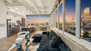 A modern kitchen with stainless steel appliances, a dining area with a black sofa and a table, and large windows offering a city view. - Dual King Suites | Skyline Views | Downtown ATL (Atlanta)