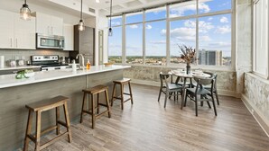 A modern kitchen with a large island, bar stools, and a dining area with a view of the city. - Dual King Suites | Skyline Views | Downtown ATL (Atlanta)
