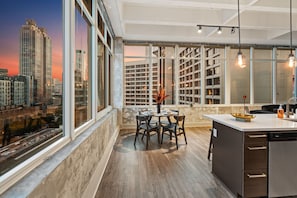 Eine moderne Küche mit einer großen Kochinsel, einem Essbereich mit Tisch und Stühlen und Blick auf eine Stadt durch große Fenster.