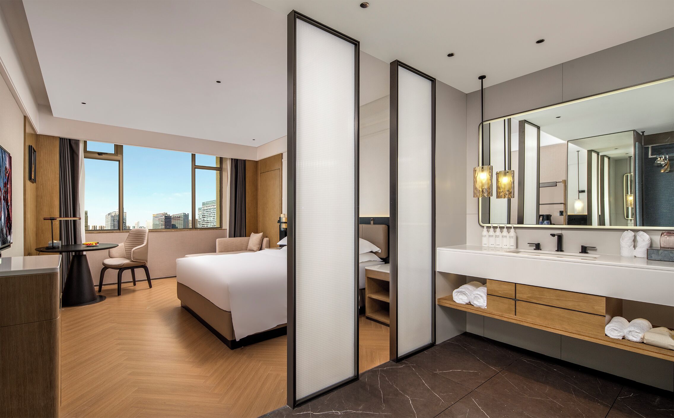 A modern hotel room with a large bed, a desk, and a bathroom with a large mirror and vanity.