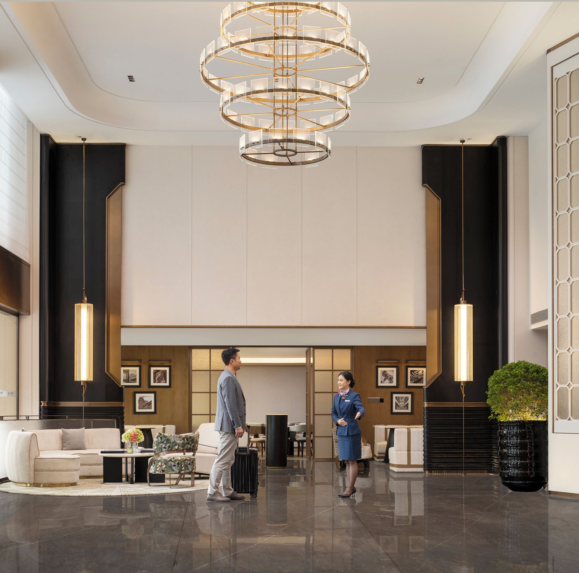 A spacious lobby with a modern chandelier, a reception desk, and a seating area with a sofa and chairs.
