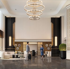 Un hall d’entrée spacieux agrémenté d’un lustre moderne, d’un comptoir de réception et d’un espace détente avec un canapé et des fauteuils.