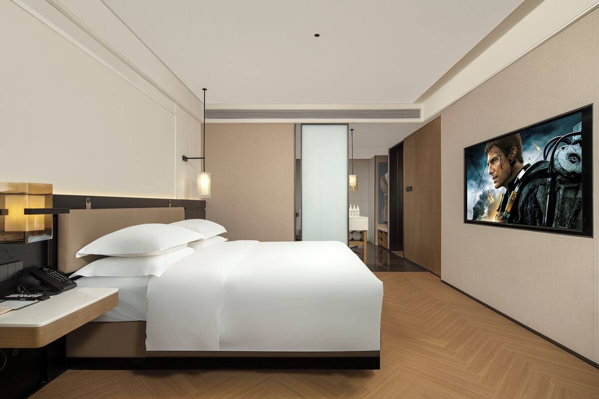 Una habitación de hotel moderna con una cama grande, una mesita de noche con teléfono y un cuadro en la pared.