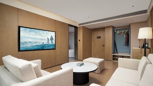 Een moderne hotelkamer met een grote flatscreen-tv, een ronde salontafel en een zithoek met twee banken.