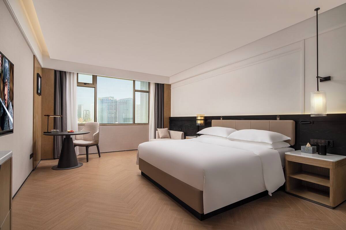 Un hotel moderno con una cama grande, un escritorio, una silla y vistas a la silueta urbana a través de amplias ventanas.
