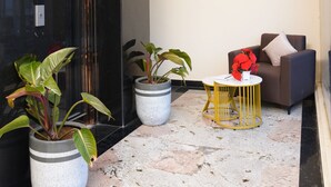 A modern lobby with a marble floor, potted plants, a seating area with a table, and a sofa.