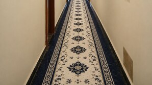A hallway with a patterned carpet, framed pictures on the walls, and a door at the end.