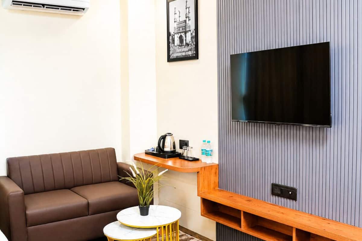 A modern living room with a brown sofa, a small round table, a TV mounted on a grey wall, and a wooden shelf below.