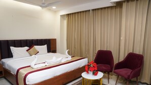 A hotel room with a bed, two red chairs, a small round table, and a curtain.