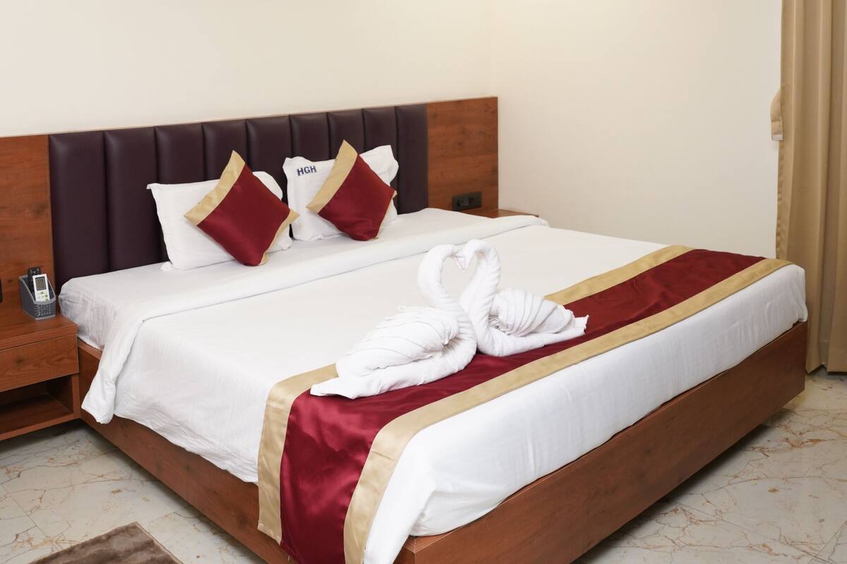 A hotel room with a wooden headboard, a bed with white and maroon bedding, a painting on the wall, and a ceiling fan.