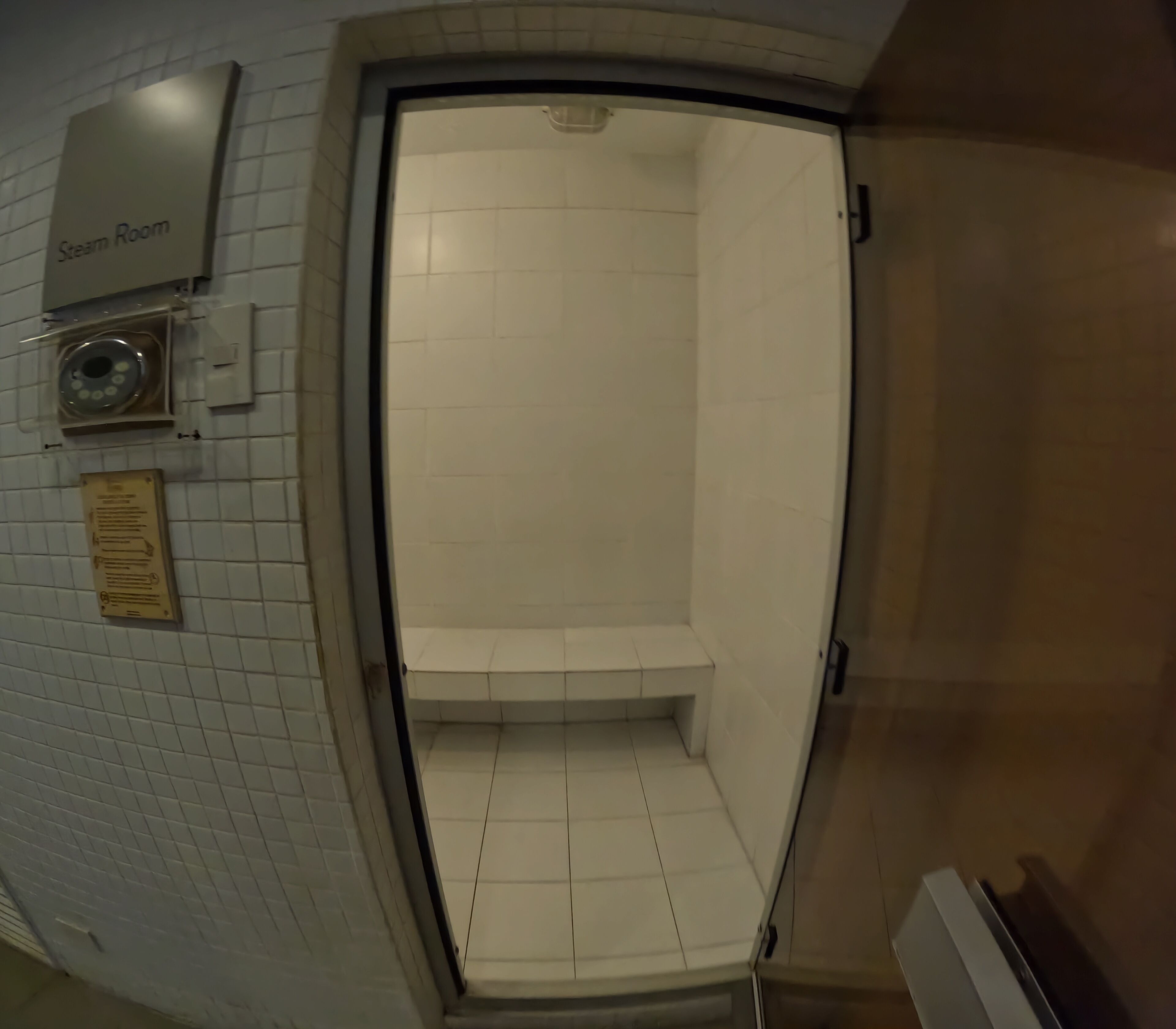 A steam room with a tiled floor, a bench, and a sign indicating its use.