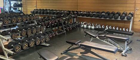A gym with weightlifting equipment, benches, and a television screen.