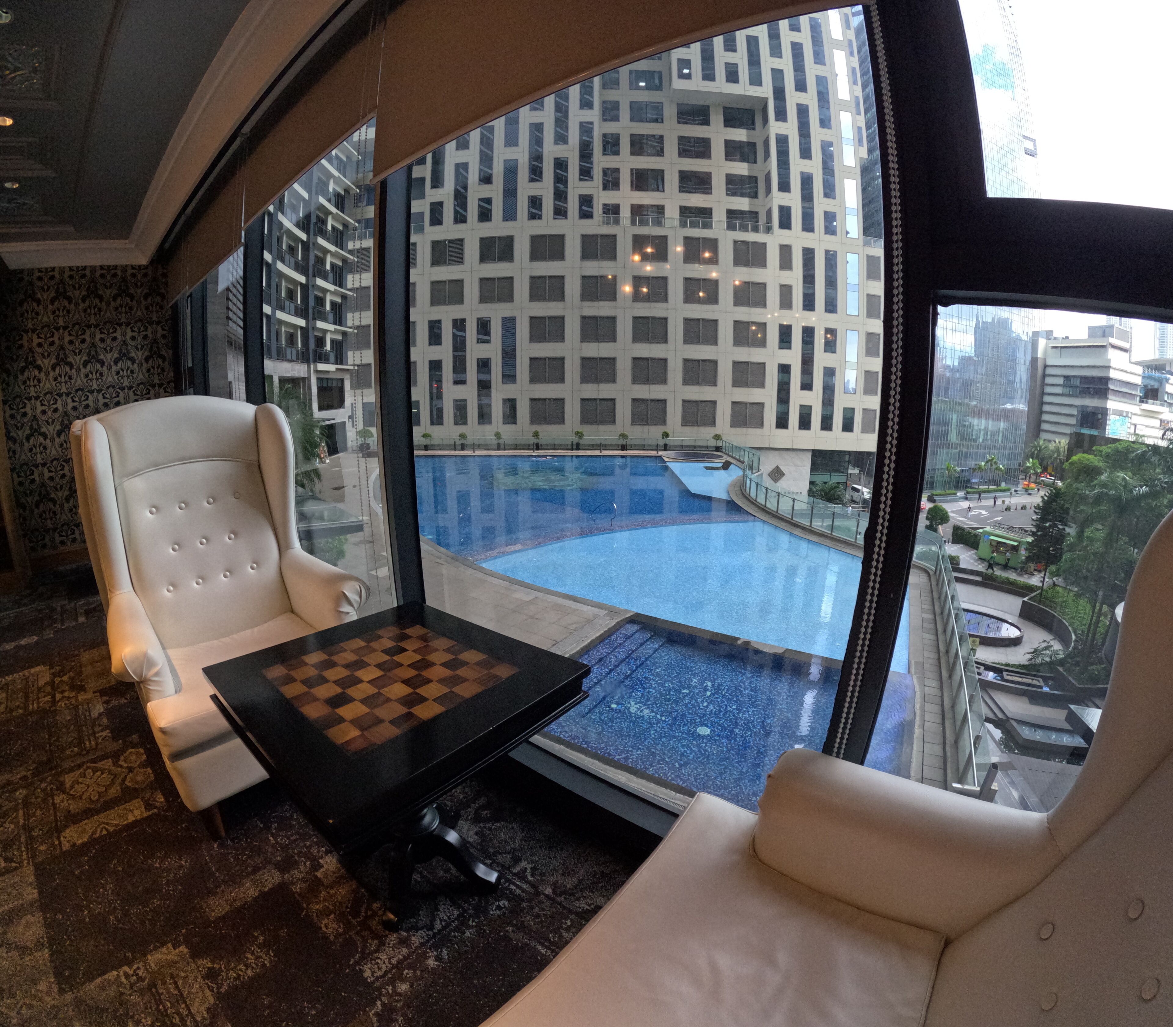 Habitación de hotel moderna con un ventanal grande, una mesa de ajedrez y dos sillones blancos.