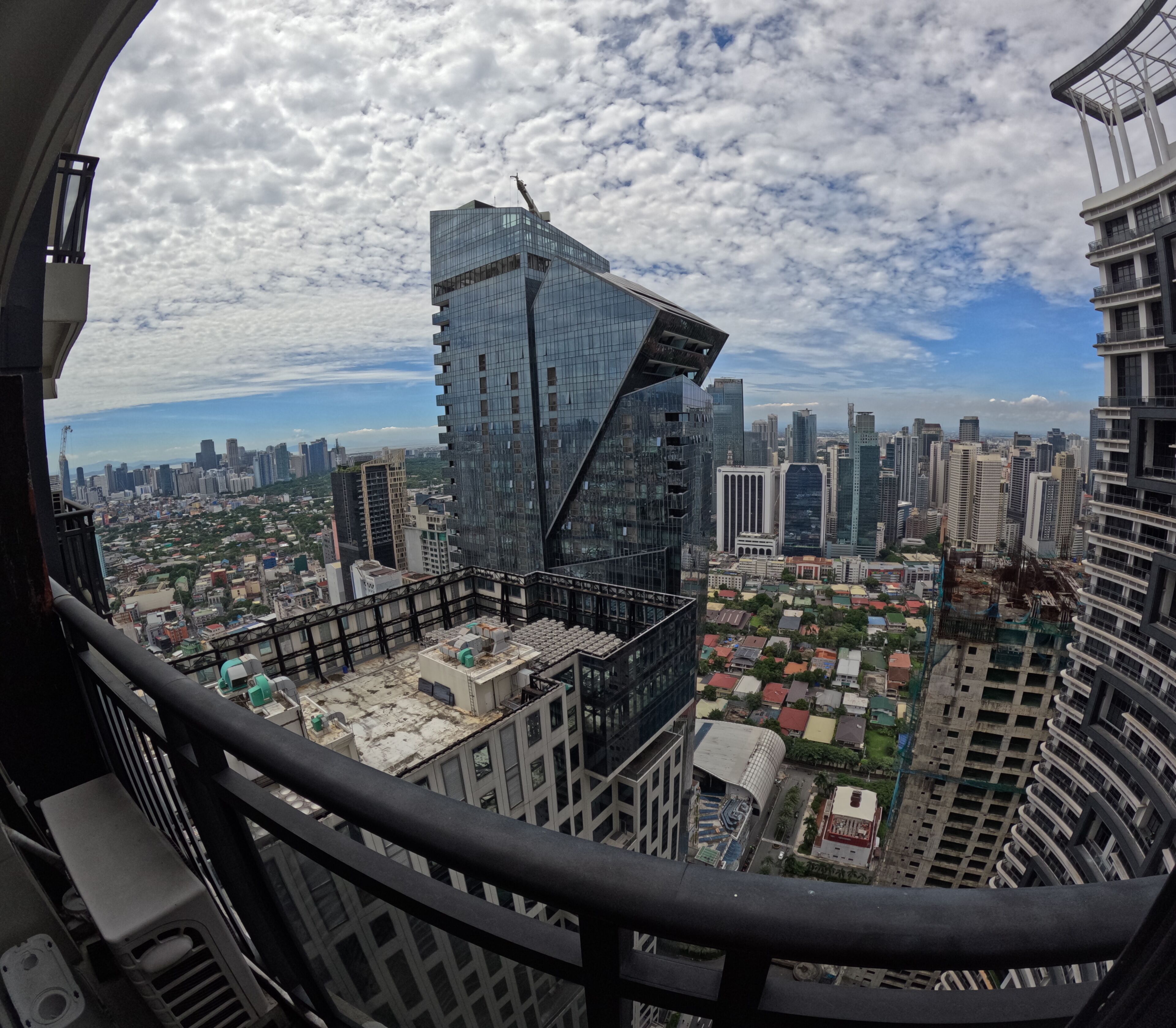 A high-rise building with a distinctive angular design, a cityscape with various buildings, and a clear sky with clouds.