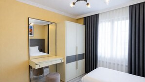 Une chambre d’hôtel comprenant un lit, une coiffeuse avec un miroir, une armoire et une grande fenêtre avec des rideaux.