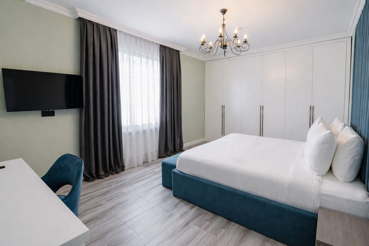Quarto de hotel moderno com uma cama grande, uma escrivaninha, uma televisão e um candelabro.