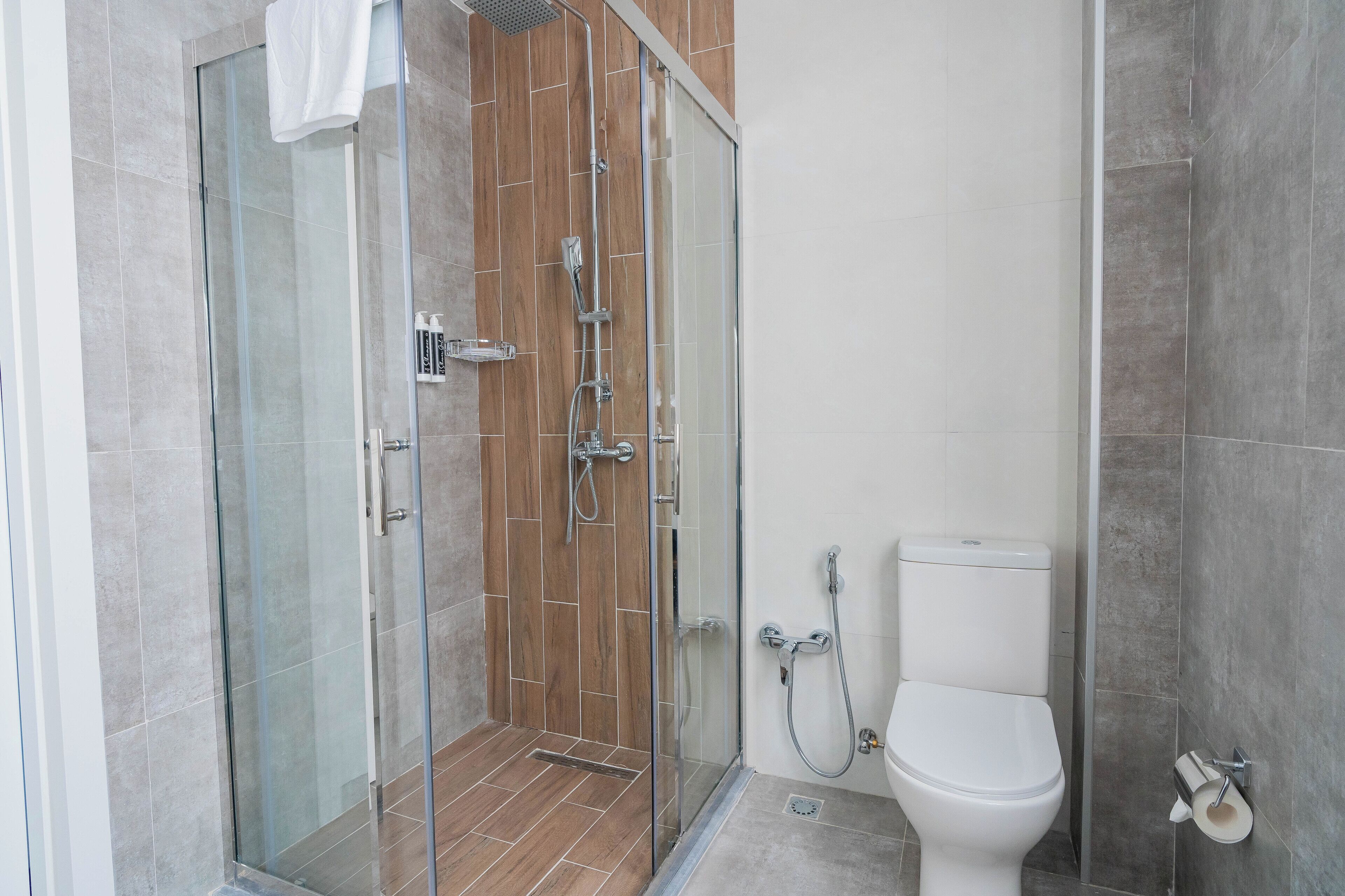 Een moderne badkamer met een douchecabine van glas, een wit toilet en een handdoek aan de douchedeur.