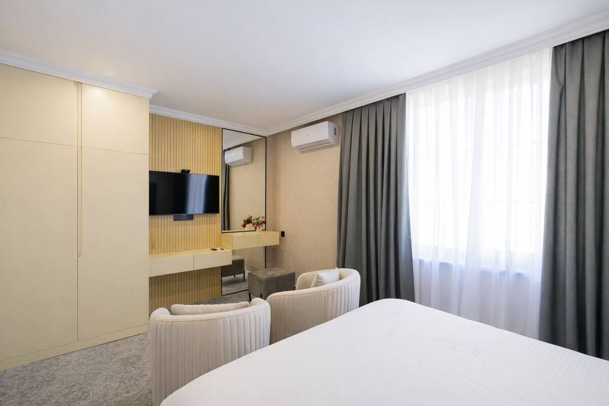 A hotel room with a bed, a desk, a chair, a TV, and a window with curtains.