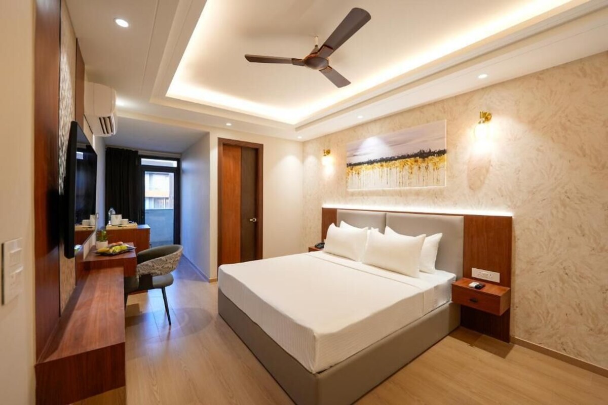 A modern hotel room with a large bed, a desk, a chair, a ceiling fan, and a wall-mounted TV.